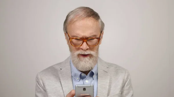 Hombre viejo molesto usando el teléfono en el estudio. Enfocado chico poniendo en gafas en el interior. — Foto de Stock