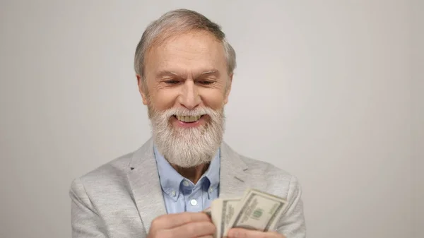 Успешный старик, имеющий деньги в студии. Улыбающийся парень считает доллары в помещении. — стоковое фото