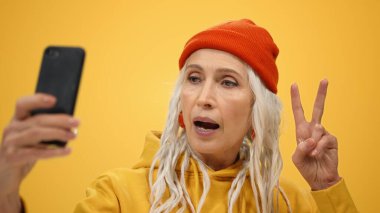 Stüdyoda kameraya poz veren neşeli yaşlı kadın. Mutlu bayan içeride selfie çekiyor..