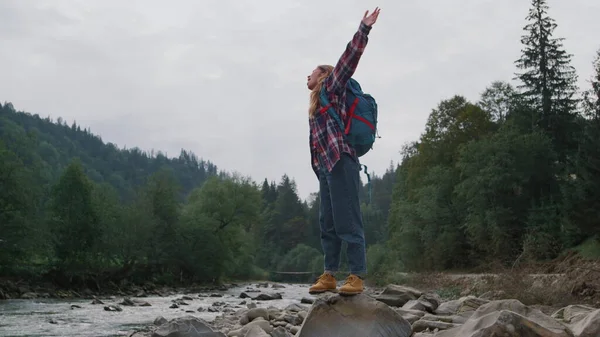 Woman raising hands in mountain landscape. Female traveler feeling freedom