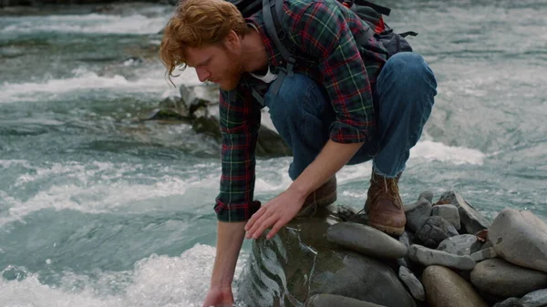 Turista seduto sulla roccia sulla riva del fiume. Uomo lavarsi le mani nel torrente di montagna — Foto Stock