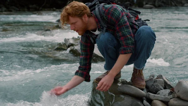 Escursionista maschio prendendo riposo al fiume in montagna. Felice ragazzo spruzzi d'acqua in aria — Foto Stock