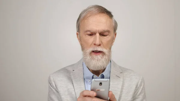 Gammal man som letar efter smartphone i studio. Gamling som använder mobiltelefon där inne. — Stockfoto