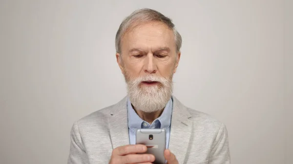 Senior man scrollend op mobiele telefoon in de studio. Verrast man met behulp van telefoon binnen. — Stockfoto