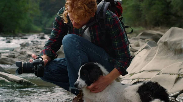 Fotografo che mostra foto di cani sulla macchina fotografica. Escursionista seduto al fiume con cane — Foto Stock