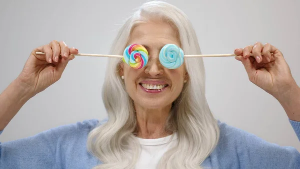 Feliz anciana sonriendo en el estudio. Vieja jugando con caramelos en el interior. — Foto de Stock