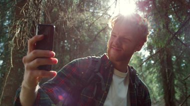 Ormanda cep telefonuyla selfie çeken bir turist. Akıllı telefona gülümseyen adam. 