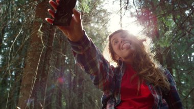 Ormanda cep telefonuyla selfie çeken bir turist. Komik suratlar yapan bir kız