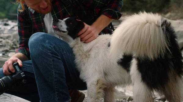 Male hiker sitting at river with dog. Redhead man petting dog — Stock Photo, Image