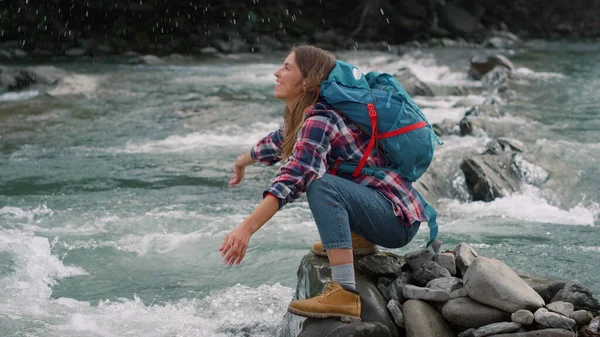 Woman sitting on shore of river. Female hiker splashing water in air from stream — Stock Photo, Image