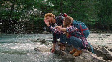 Nehir kıyısında oturan kadın ve adam. Nehirden su sıçrayan yürüyüşçüler