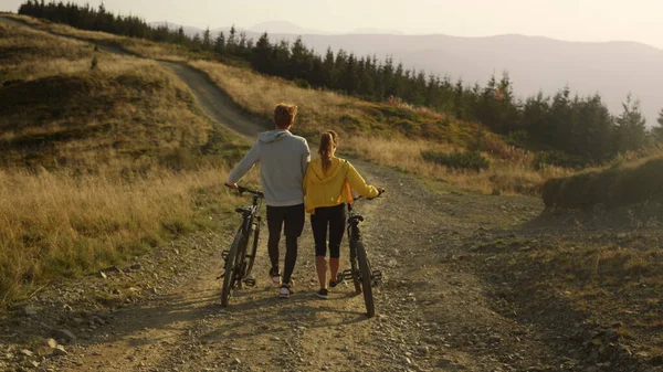 Mujer y hombre con bicicletas caminando por la carretera. Pareja tomando un descanso después del ciclismo — Foto de Stock