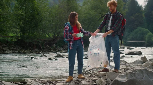 Voluntários coletando garrafas no saco. Turistas limpando rio de resíduos humanos — Fotografia de Stock