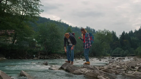 Пара стоящих на скалистом берегу реки. Туристы касаются воды в реке — стоковое фото