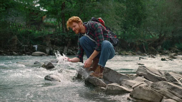 Viandante maschio in pausa al fiume durante l'escursione. Redhead uomo spruzzi d'acqua — Foto Stock