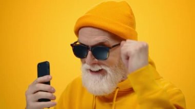 Olgun adam içeride dans ediyor. Telefonu olan neşeli yaşlı adam içeride eğleniyor..