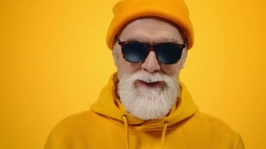 Neşeli yaşlı adam içeride el kaldırıyor. Stüdyoda kameraya poz veren neşeli adam..