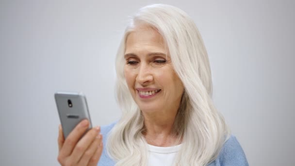 Senior vrouw scrollen online binnen. volwassen dame kijken nieuws in mobiele telefoon. — Stockvideo