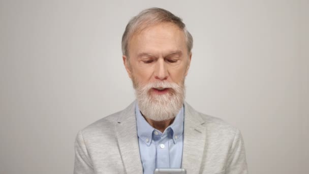 Ανώτερος άνθρωπος ψάχνει smartphone μέσα. Συγκεντρωμένος κύριος διαβάζει ειδήσεις στο στούντιο — Αρχείο Βίντεο