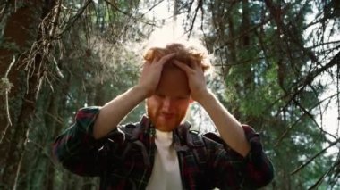 Yeşil ormanda duran kızıl saçlı adam. Saçına elleriyle dokunan yakışıklı adam.