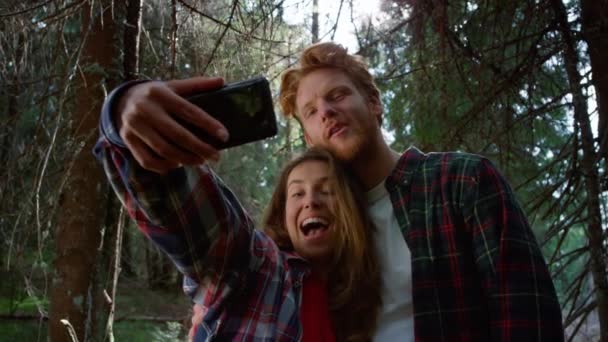 Amigos tomando selfie en smartphone en el bosque. Hombre y mujer haciendo caras graciosas — Vídeo de stock