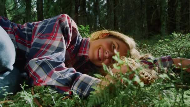 Ormanda yeşil çimlerin üzerinde yatan bir kız. Neşeli kadın eğreltiotu yapraklarına dokunuyor — Stok video