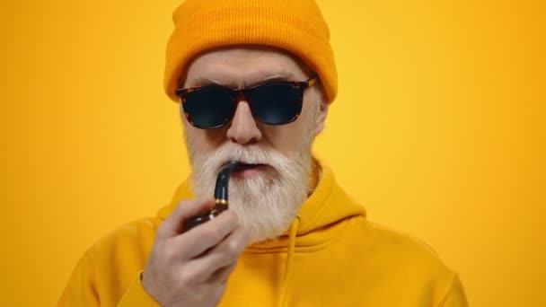 Rich old man smoking pipe indoors. Senior guy holding pipe in mouth in studio. — Stock Video
