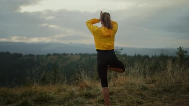 Fit Mädchen üben Yoga-Pose in den Bergen. Frau steht in Baumpose auf Gras — Stockvideo