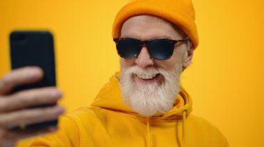 İçeride kameraya poz veren neşeli, yaşlı bir adam. Yaşlı adam stüdyoda selfie çekiyor..