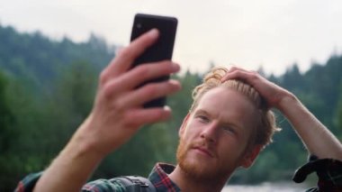 Adam selfie 'den önce saç stilini düzeltiyor. Dağlarda akıllı telefondan selfie çeken adam.