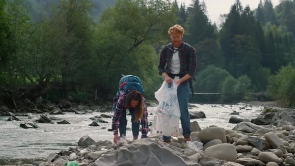 Voluntarios recogiendo botellas de plástico en la orilla del río. Pareja recogiendo basura — Vídeo de stock