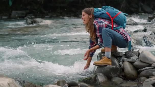 Mulher a fazer uma pausa no rio nas montanhas. Menina feliz salpicando água no ar — Vídeo de Stock