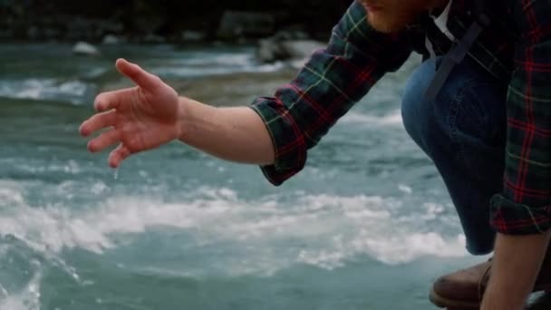 Turista tomando un descanso durante la caminata en el río. Hombre tocando agua clara con la mano — Vídeo de stock