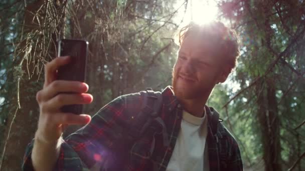Турист делает селфи на мобильном телефоне в лесу. Парень улыбается смартфону — стоковое видео