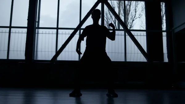 Silhouette of dancer practicing in dark interior. Unknown man dancing indoors.