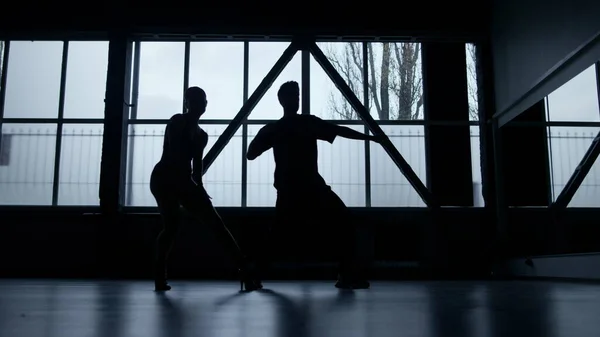 Silhouette dancers performing hip hop in dark studio. Guy and girl dancing .