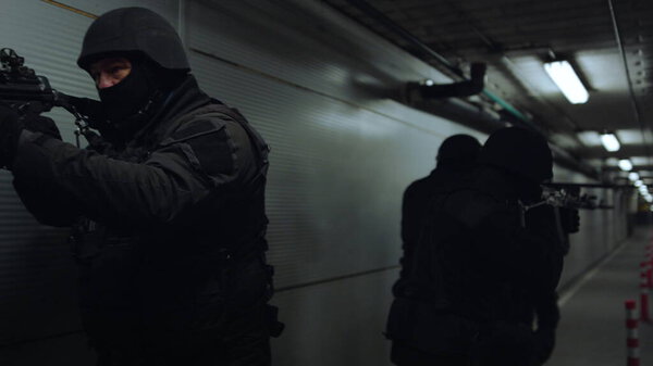 SWAT team walking in dark corridor. Special forces group pointing weapons
