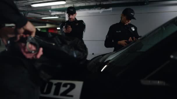 駐車場で犯罪者を逮捕する警察チーム。パトロールカーの警官の手錠容疑者 — ストック動画