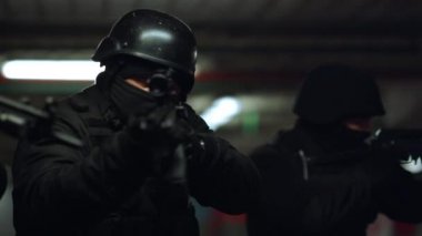 Özel harekat polisi otoparkı araştırıyor. SWAT subayları tüfekleri doğrultuyor.