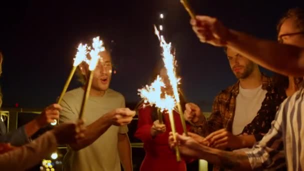 Multiethnische Freunde genießen Geburtstagsparty auf dem Dach. Menschen verbrennen Wunderkerzen. — Stockvideo