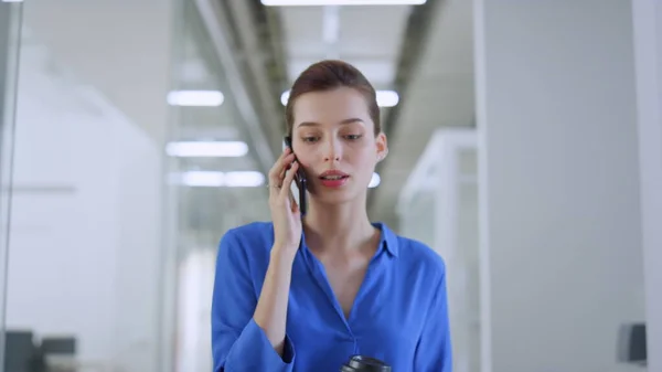 Een vrouw die binnen over een mobieltje praat. Zakelijk meisje gaat met papieren beker kantoor — Stockfoto