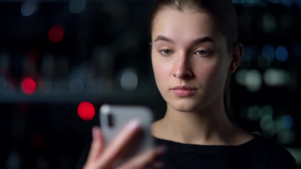 Porträt eines ernsthaften Mädchens, das ein Selfie auf einem Smartphone mit nächtlichem Hintergrund macht. — Stockvideo