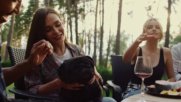 Happy people having rest on grill party outside. Smiling woman playing with dog