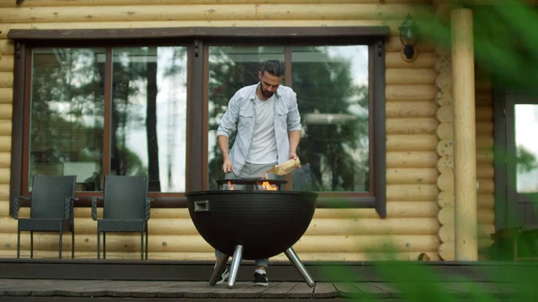 Homme réfléchi mettre du bois de chauffage dans barbecue grill. Focalisé gars faire le feu dans le gril — Photo