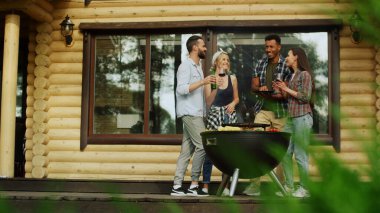 Çok ırklı arkadaşlar dışarıda parti yapıyorlar. İnsanlar evin yakınında sohbet ediyorlar.