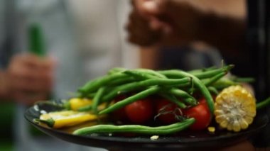 Yakından Fransız fasulyesi, domates, biber ve mısır. Tabak tutan adam