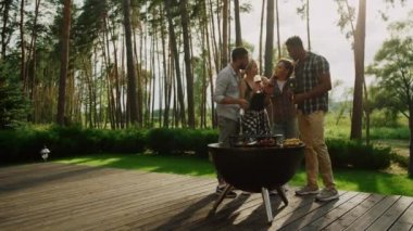 Çok ırklı arkadaşlar dışarıda barbekü partisinde dinleniyorlar. İnsanlar bbq yemeği pişiriyor.
