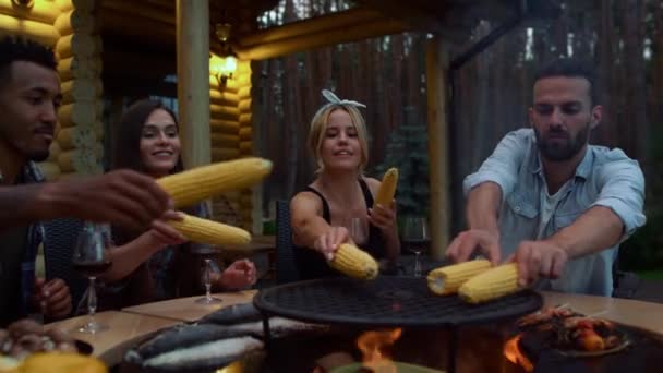 Joyful people preparing frying corn outside. Fellows putting corn on bbq grill — Stock Video