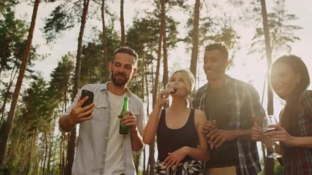 Amigos juguetones tintineando vasos con teléfono al aire libre. Compañeros descansando en la fiesta. — Vídeos de Stock