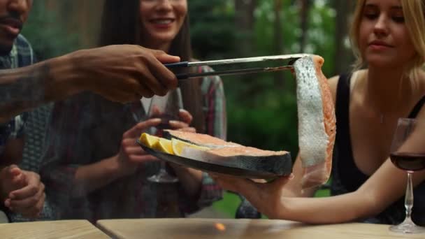 Skupiona kobieta pomaga szefowi kuchni na podwórku. Człowiek ręce kładąc kawałek ryby na grillu — Wideo stockowe